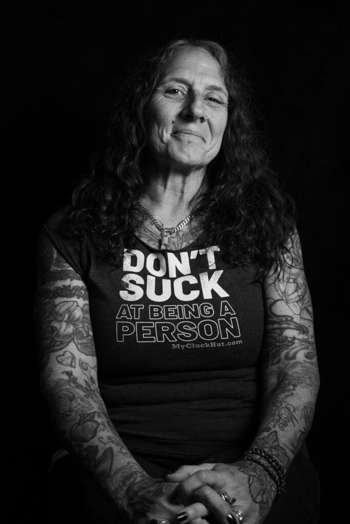 Tattooed person profile picture Anne Morando wearing a message shirt that says don't suck at being a person.